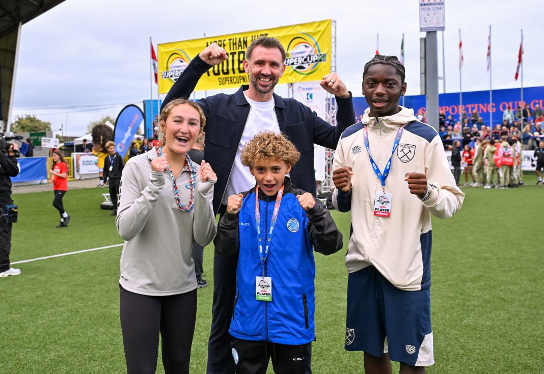 Madisyn Tiano (New York Rush Select), Concilio Tonebi (West Ham), and Roman Gaglio (IDA Bermuda) pictured with Northern Ireland football icon Gareth McAuley MBE as they officially kicked off the 2025 Budget Energy SuperCupNI in front of a packed crowd at Coleraine Showgrounds.
